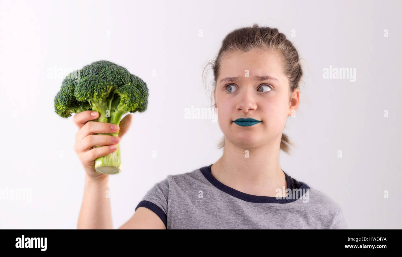A pretty girl skeptically holds a broccoli in her hand Stock Photo