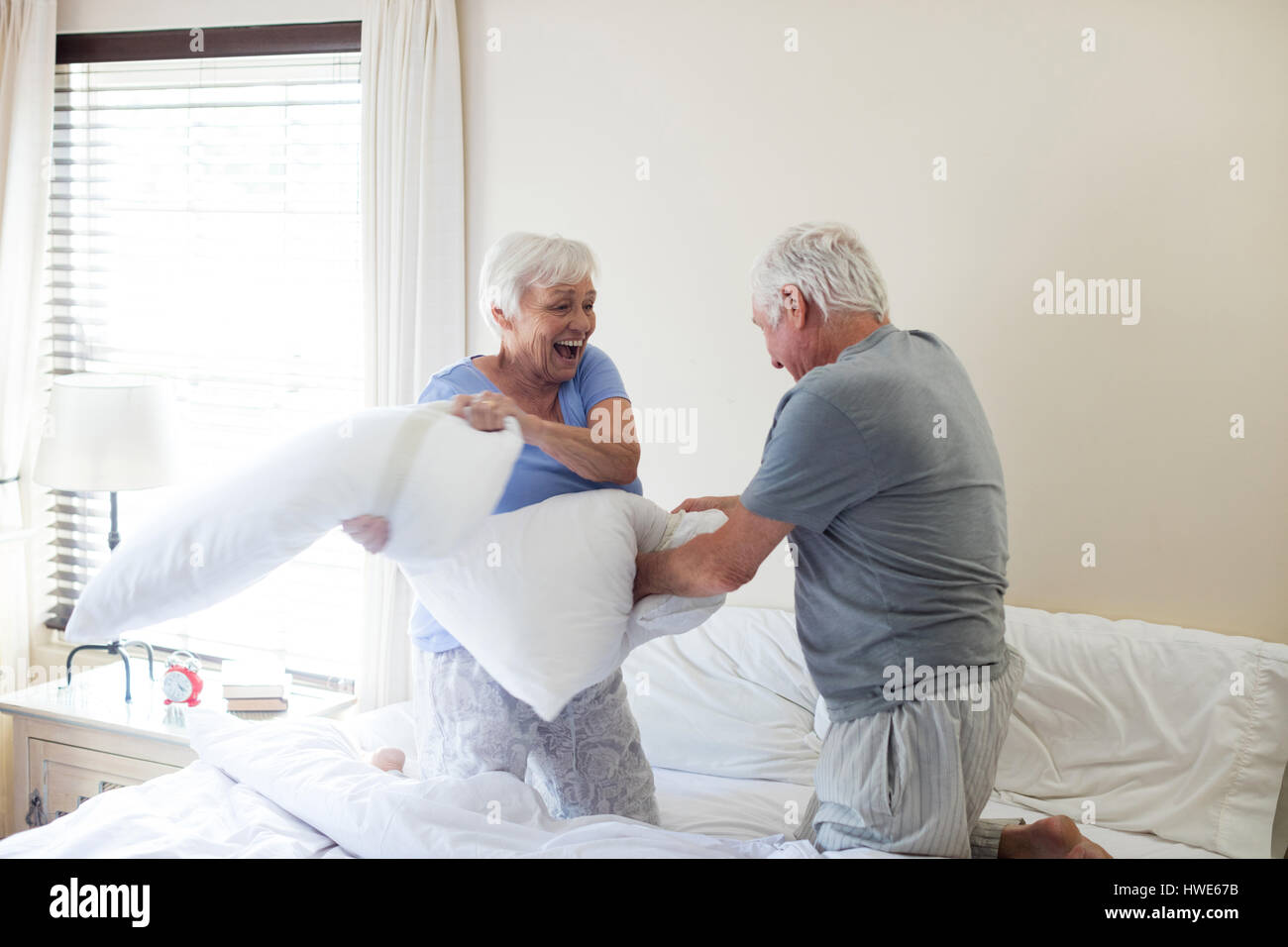 Senior couple having pillow fight on bed in bedroom Stock Photo