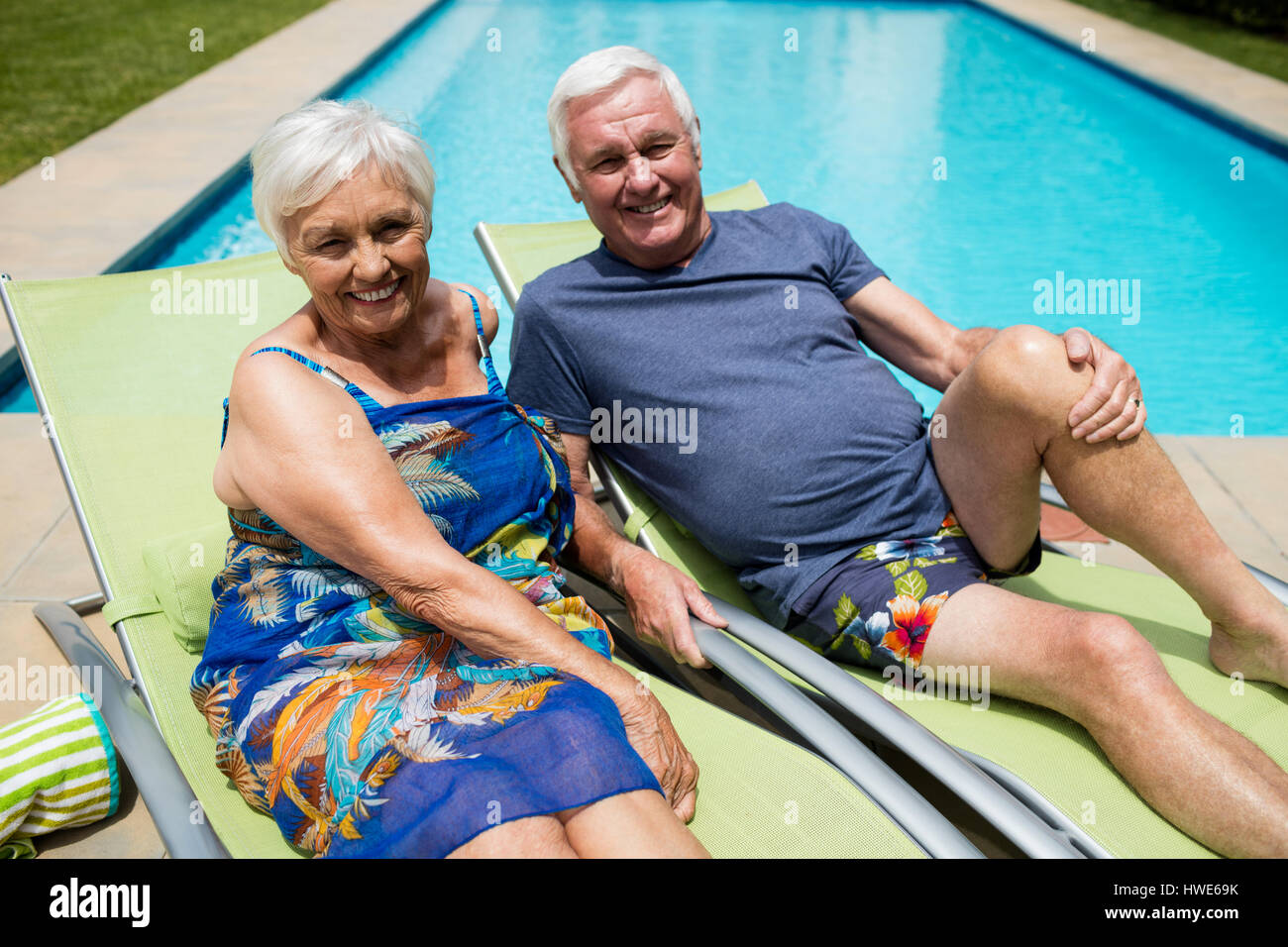 Portrait of senior couple relaxing on lounge chair at poolside Stock ...