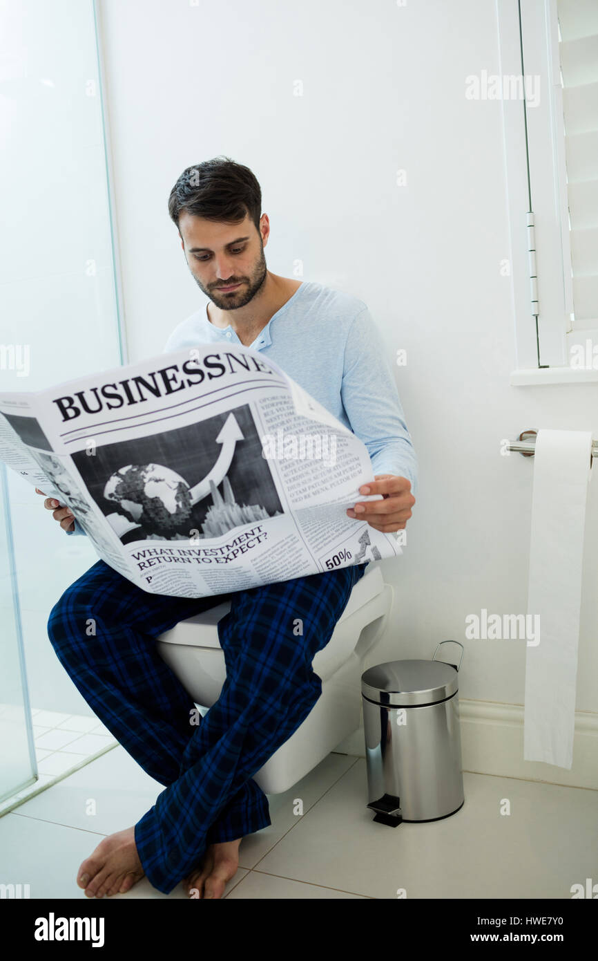 Man sitting on toilet seat reading a newspaper at home Stock Photo