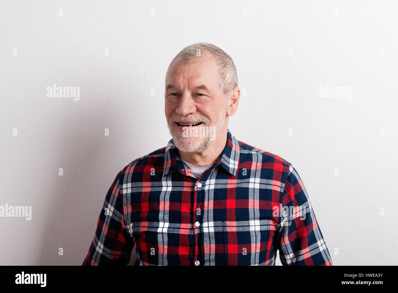 Senior man in checked shirt smiling, studio shot against white w Stock Photo