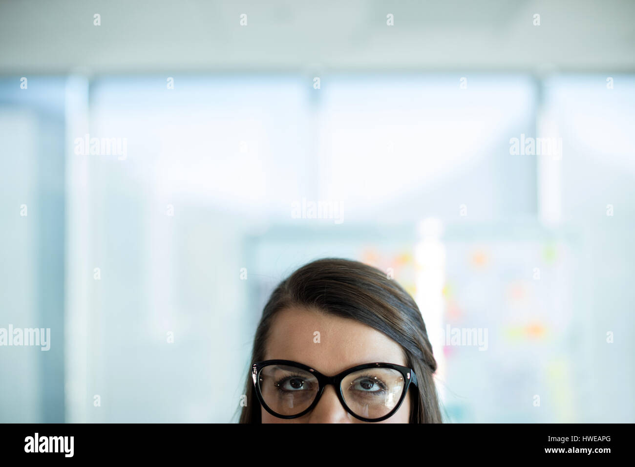 Woman in spectacles glancing upwards in office Stock Photo