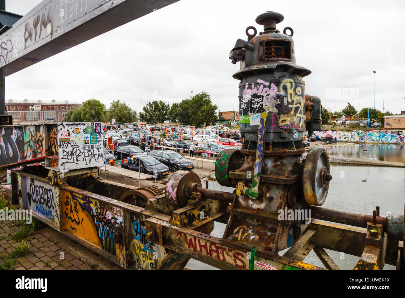 Graffiti scrawled over derelit machinery on the NDSM wharf in Amsterdam.  A regular fleamarket can be seen in the background Stock Photo