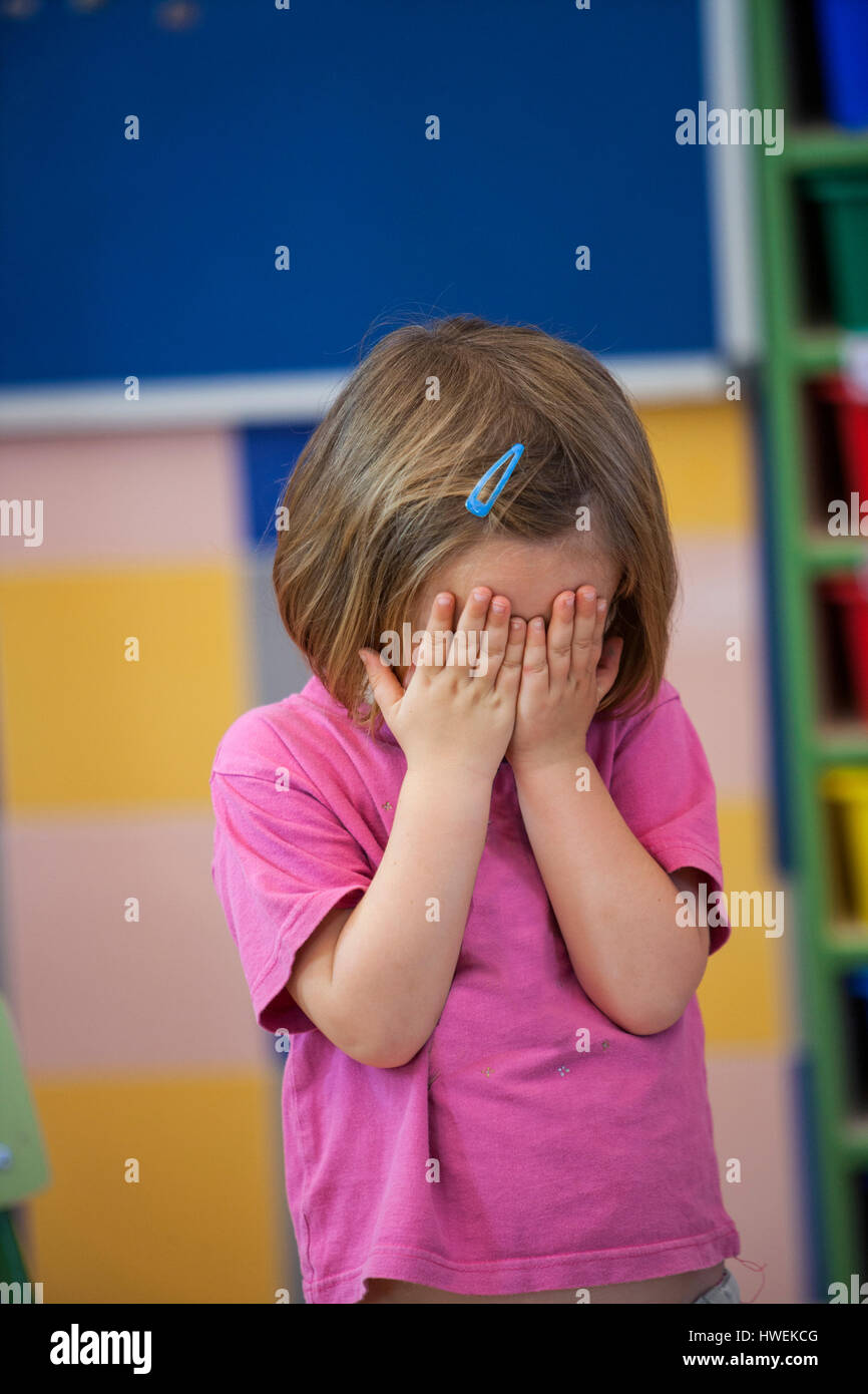 Preschool girl covering her eyes with hands in classroom Stock Photo