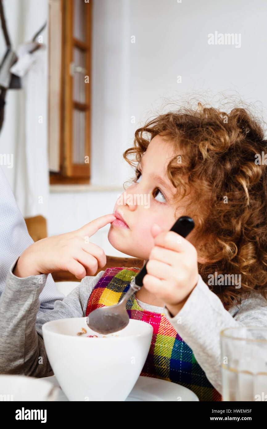 Girl looking up while having cereal in kitchen Stock Photo