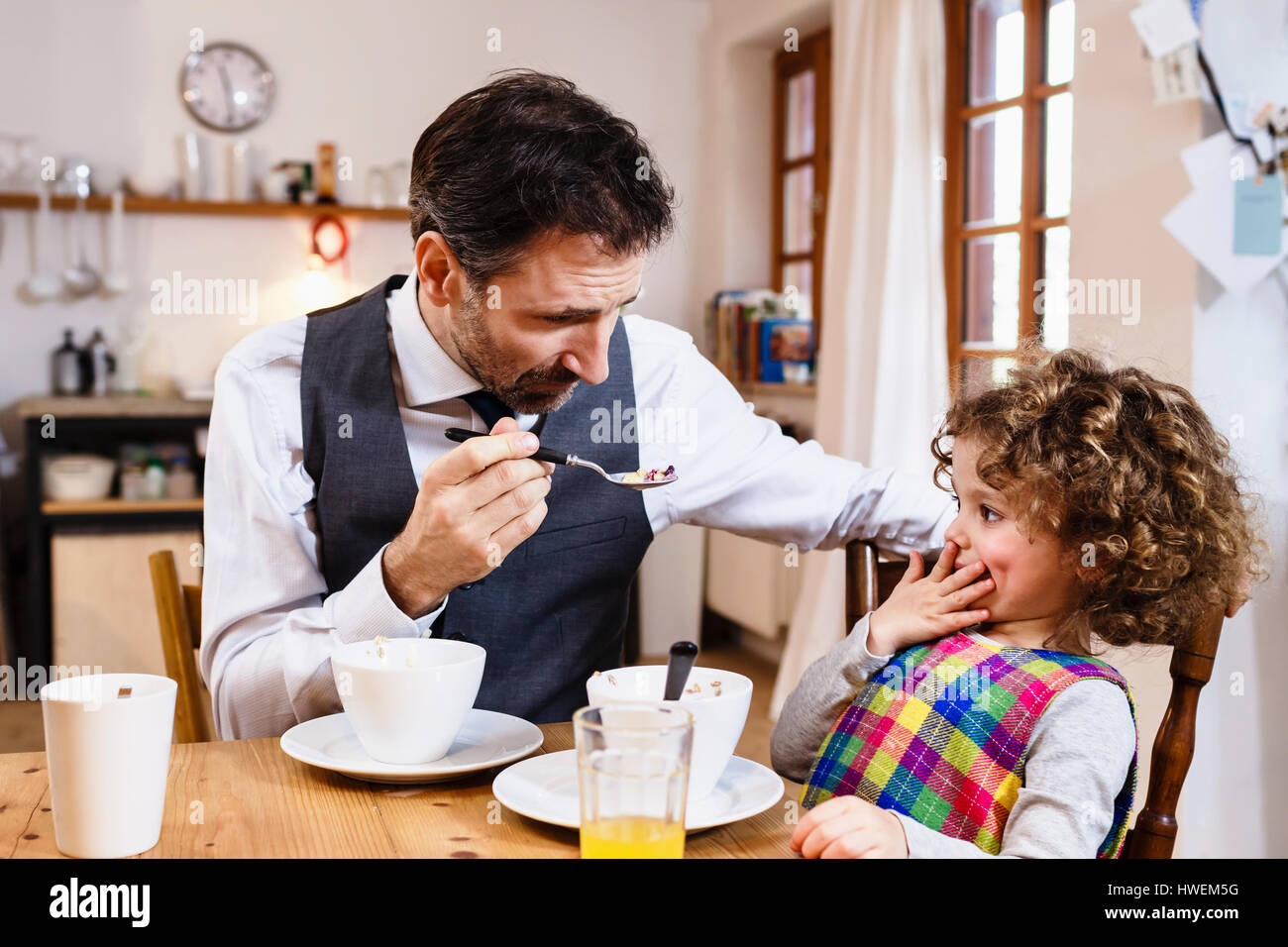 Man feeding daughter cereal with hand over mouth in kitchen Stock Photo