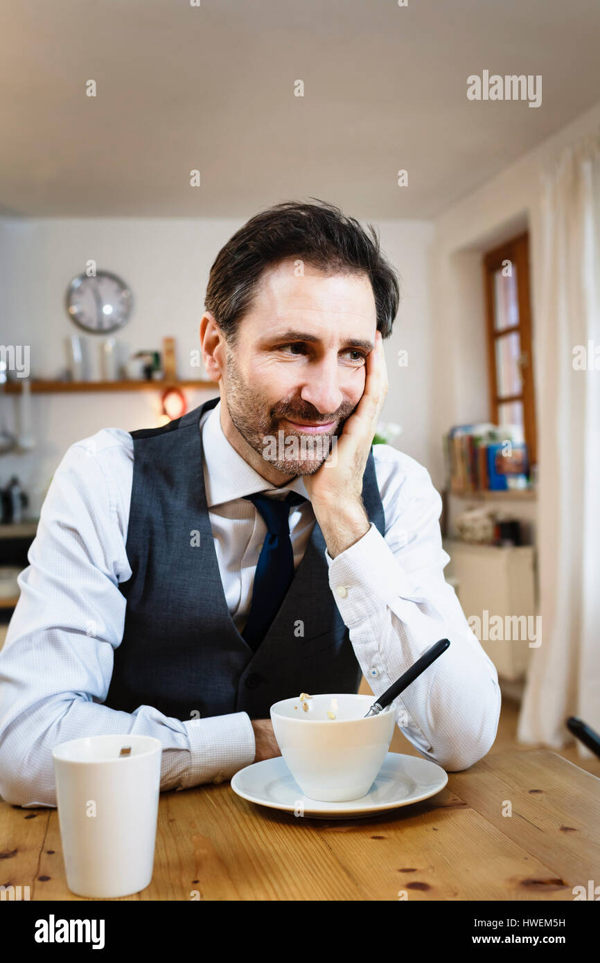 Smiling mature man with chin on hand at breakfast in kitchen Stock Photo