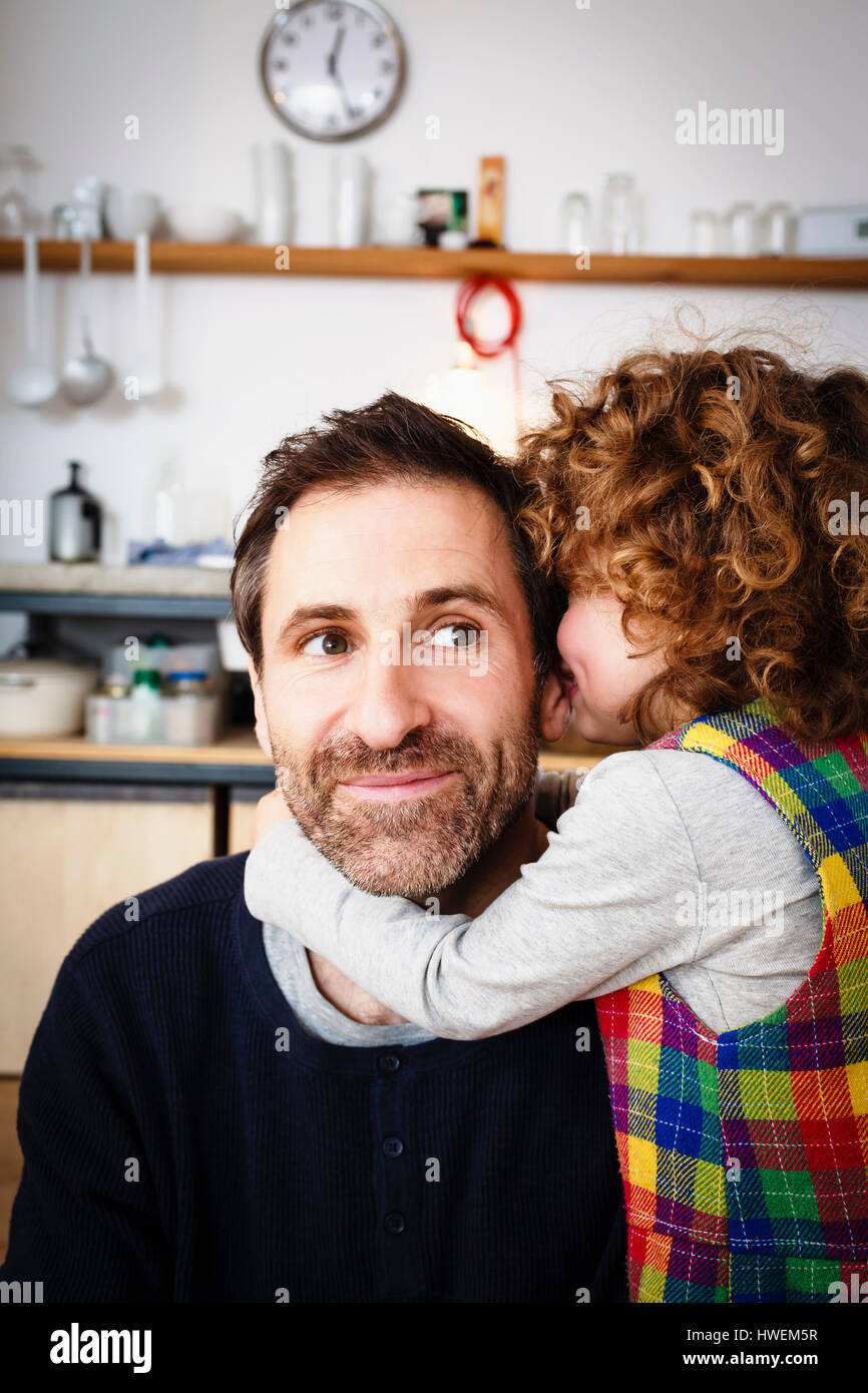 Girl whispering to father in kitchen Stock Photo