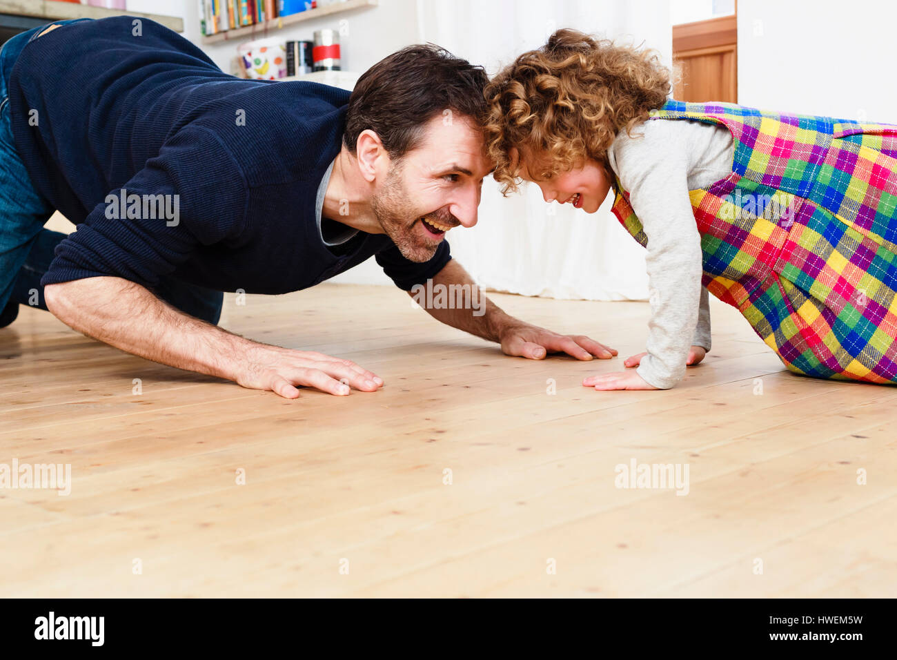 Mature man crawling head to head with daughter on kitchen floor Stock Photo