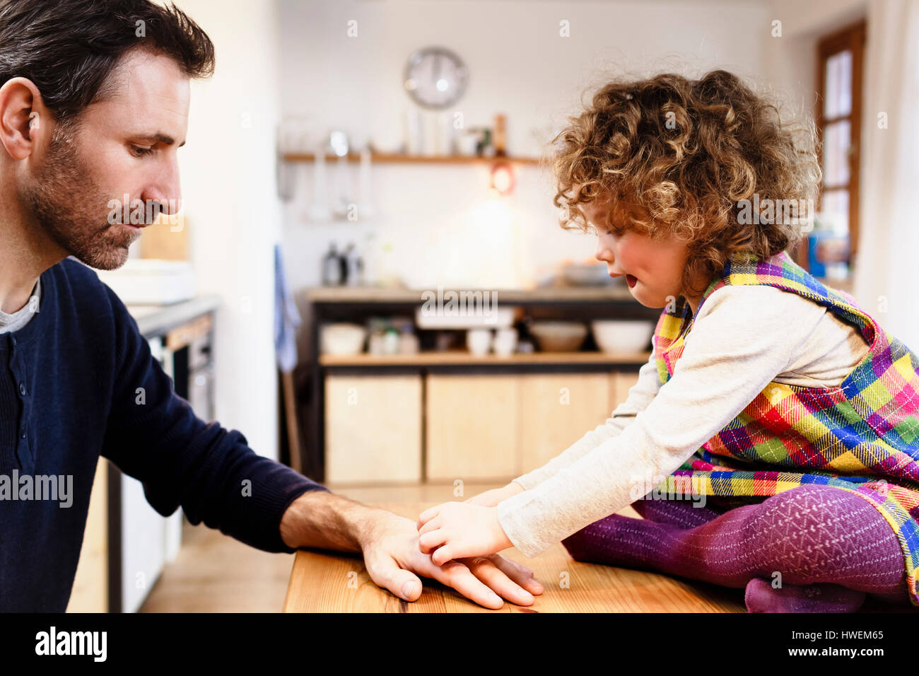 Girl on table sticking adhesive plaster onto father's hand Stock Photo