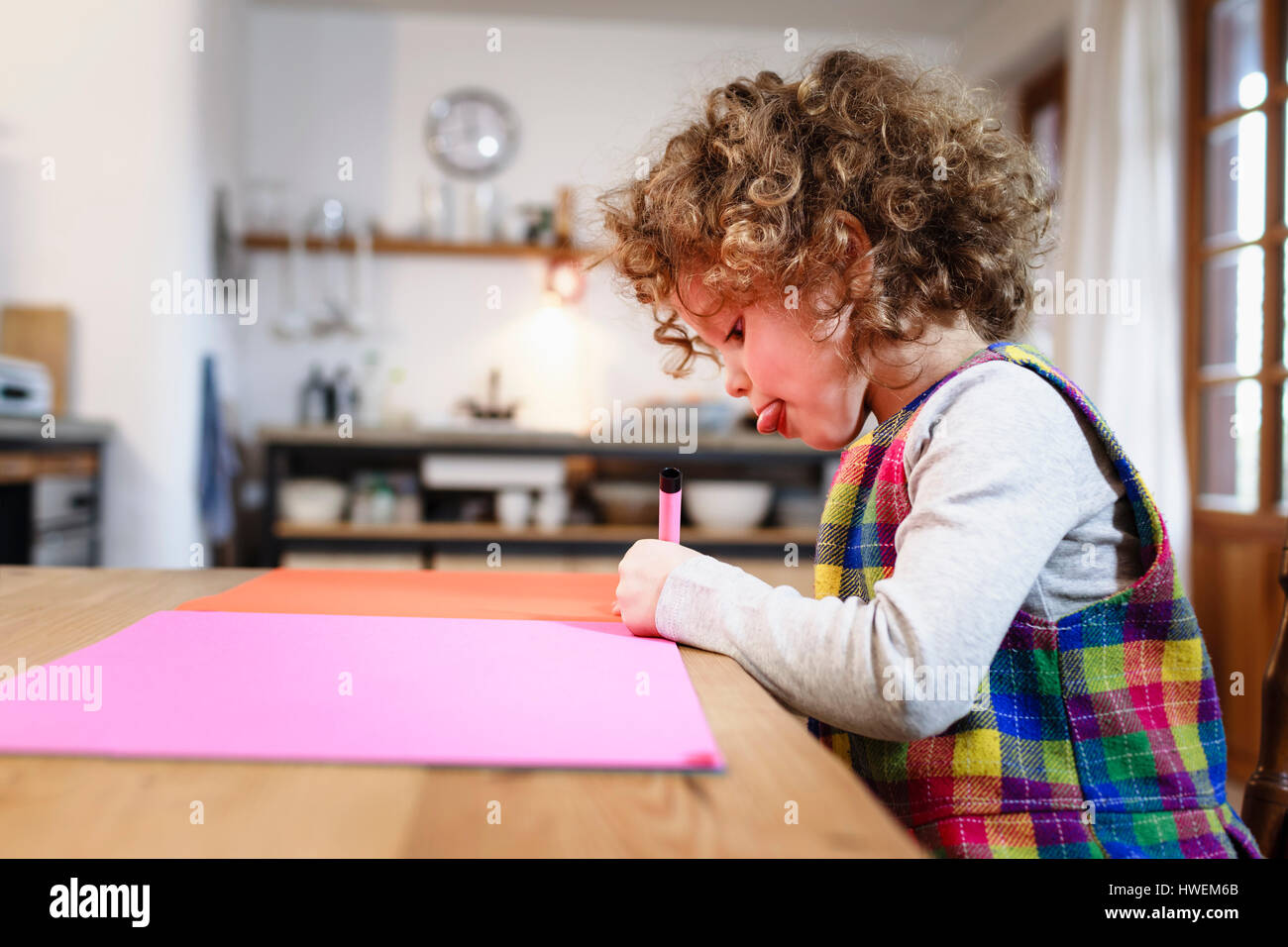 Girl drawing on pink paper at table Stock Photo
