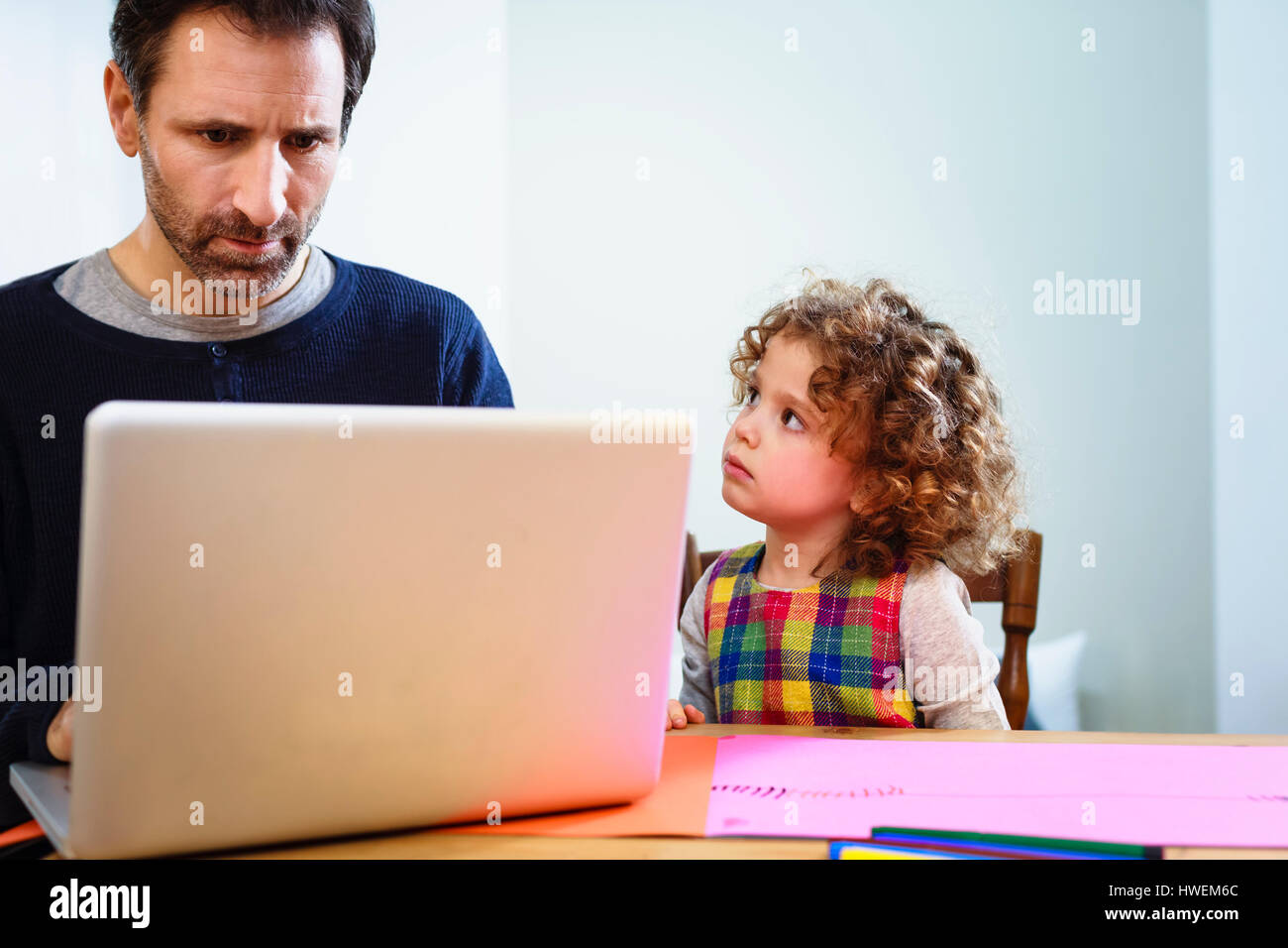 Girl staring at father using laptop at table Stock Photo