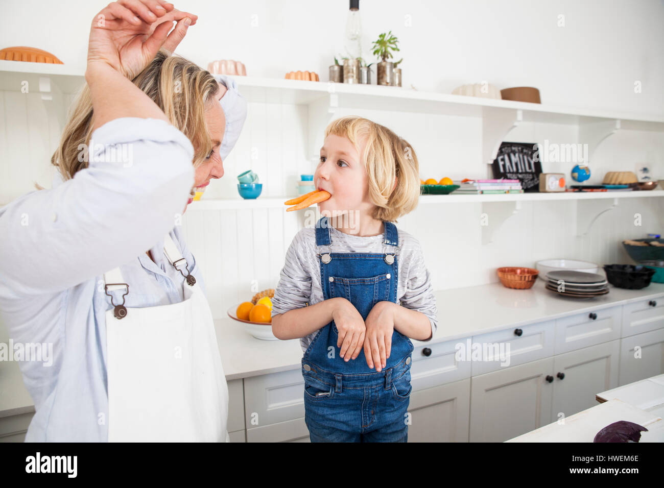 Mature woman and daughter mimicking rabbits with carrots in kitchen Stock Photo