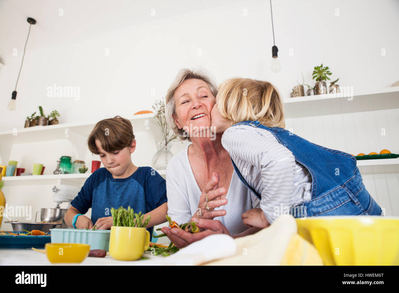 Girl kissing grandmother while preparing fresh vegetables at kitchen table Stock Photo