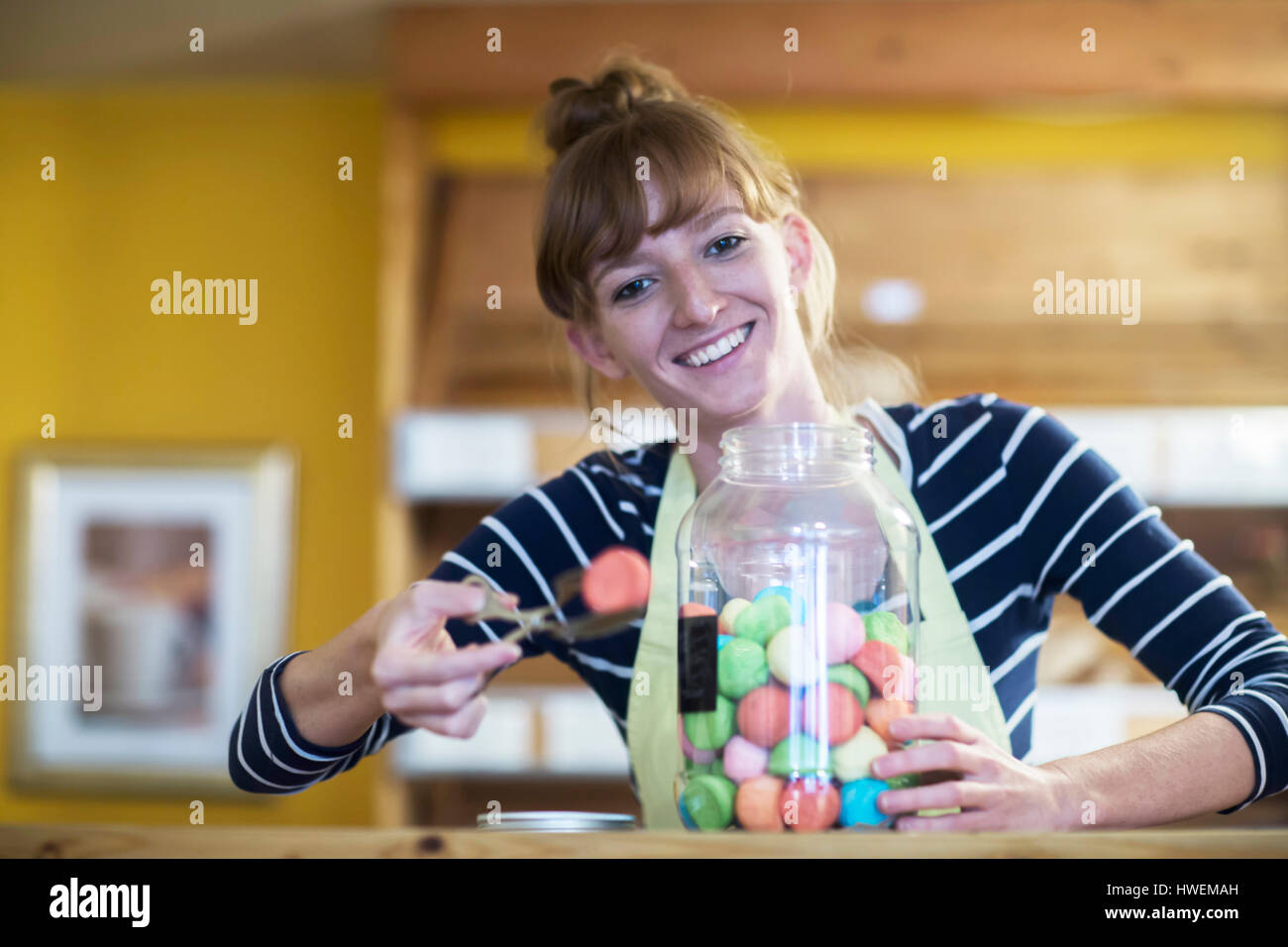 Portrait of young woman in food shop, taking sweet food from jar Stock Photo