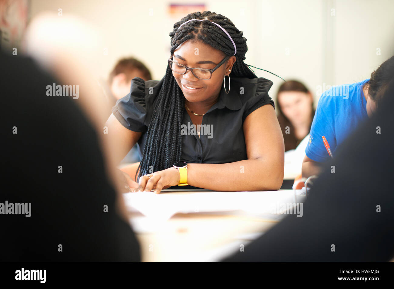 Teenage female student writing at desk in college classroom Stock Photo