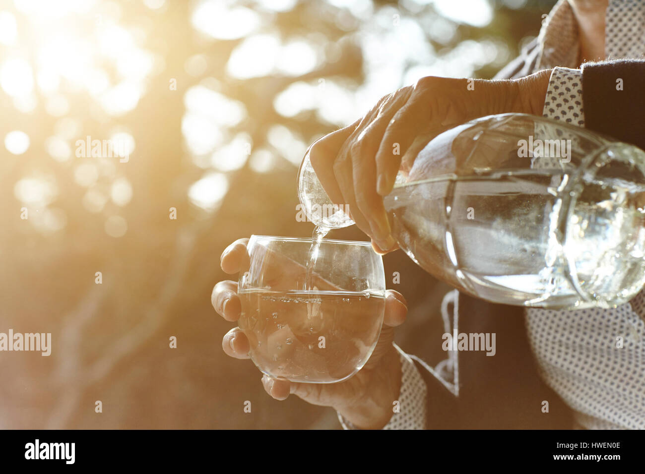 Hands of senior woman pouring glass of water by window Stock Photo