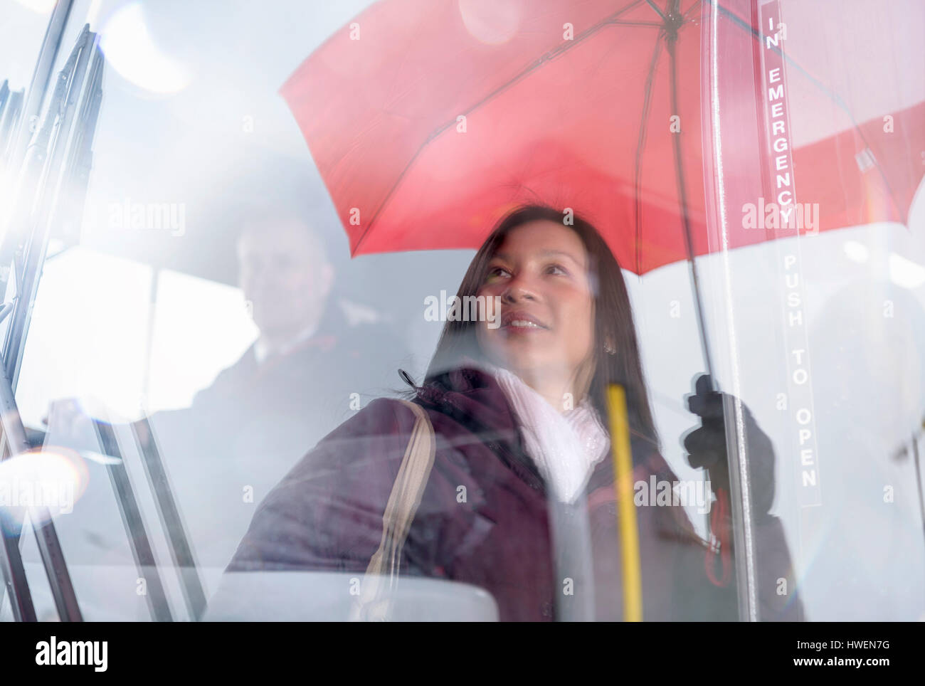 Passenger with umbrella reflected in windscreen of electric bus Stock Photo