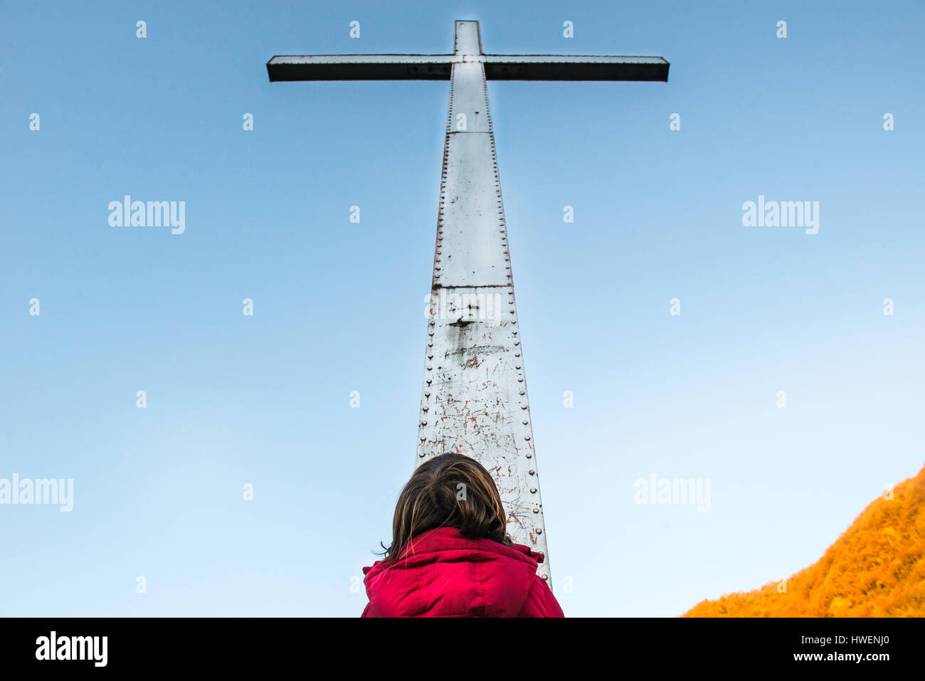 Rear view of boy looking up at towering cross and blue sky Stock Photo