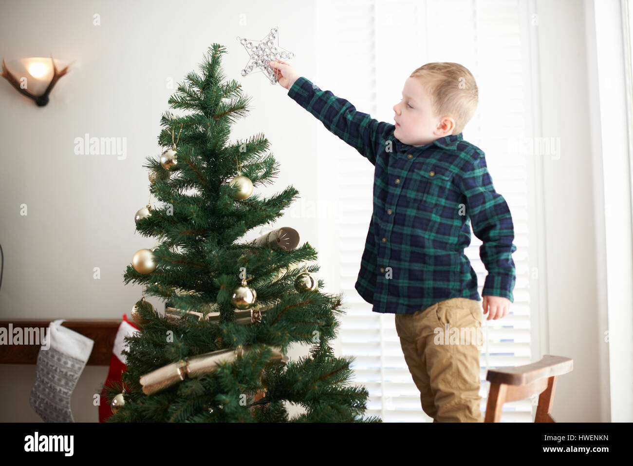 Boy standing on chair to place star on christmas tree Stock Photo