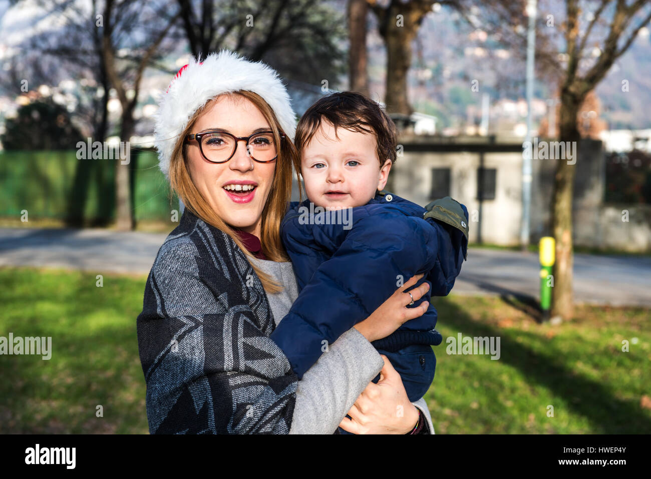 Portrait of young woman in santa hat carrying baby boy in park Stock Photo