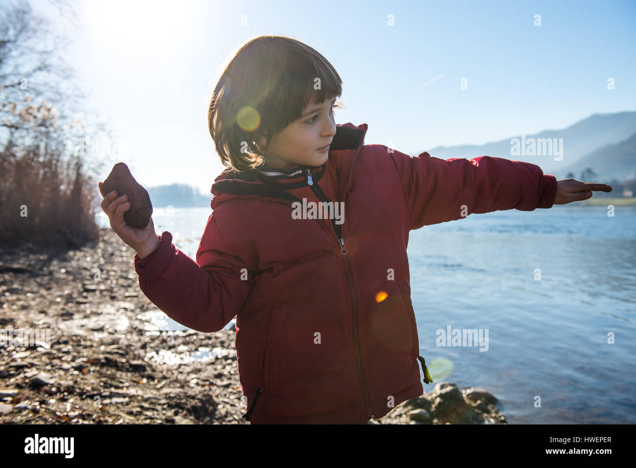 Young boy beside lake, throwing stone into lake Stock Photo