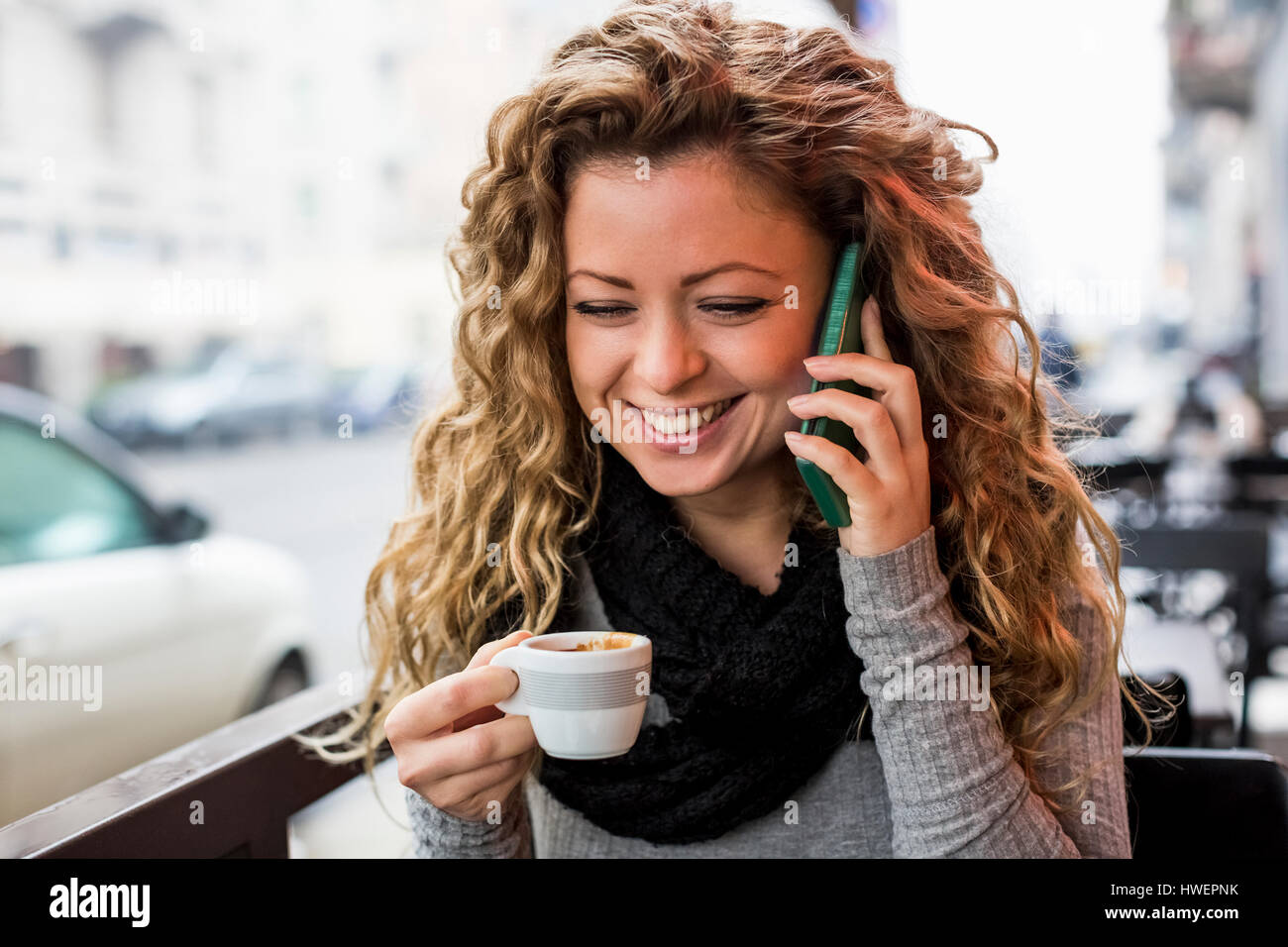 Woman in cafe holding espresso cup making telephone call smiling Stock