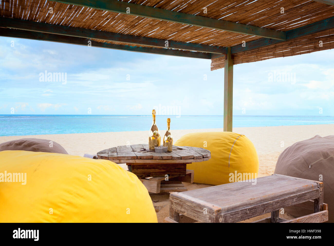 Two bottles of champagne on an old wooden table with pouf seats for romantic  dinner for honeymoon copules on a tropical beach Stock Photo