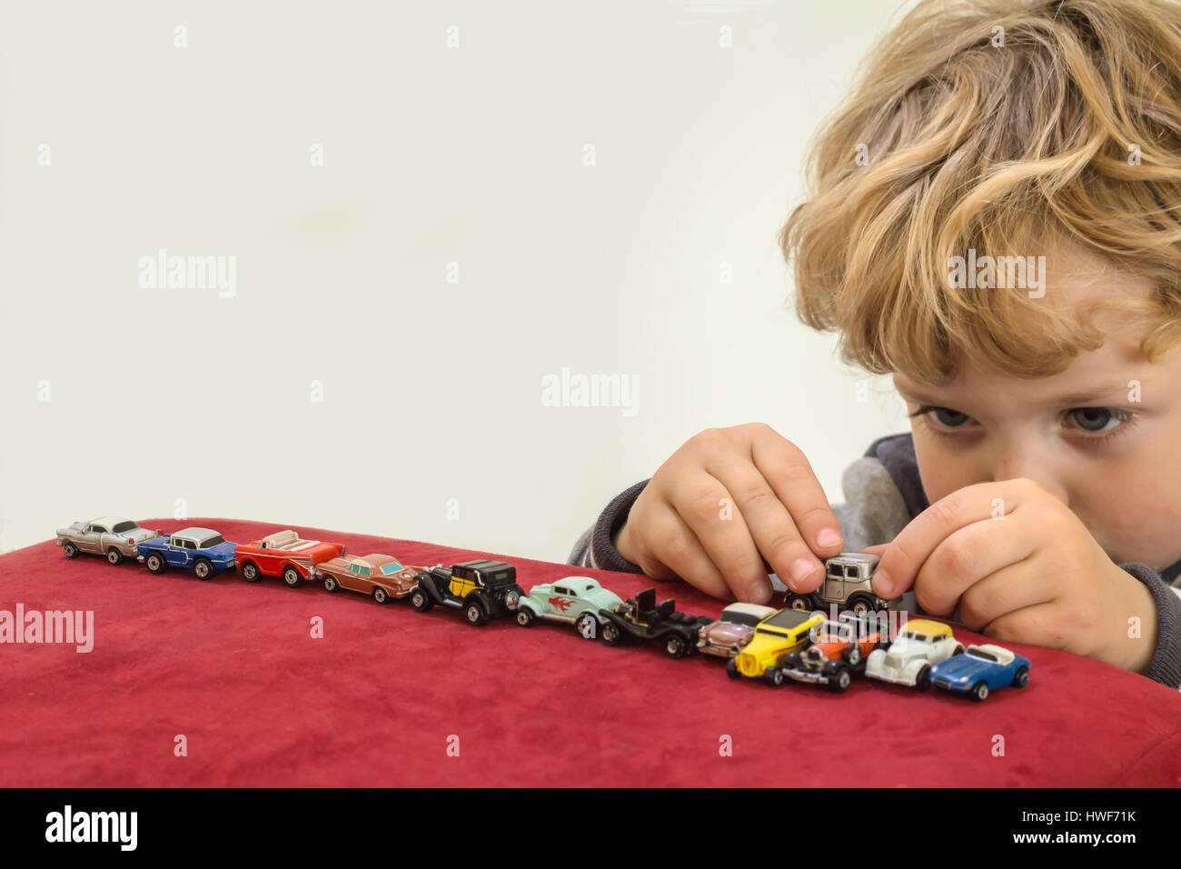 QUEENSTOWN, SOUTH AFRICA - MAY 17 2015 - Little blonde boy playing with vintage toy cars on red velvet pouf chair - Editorial Illustrative Image Stock Photo