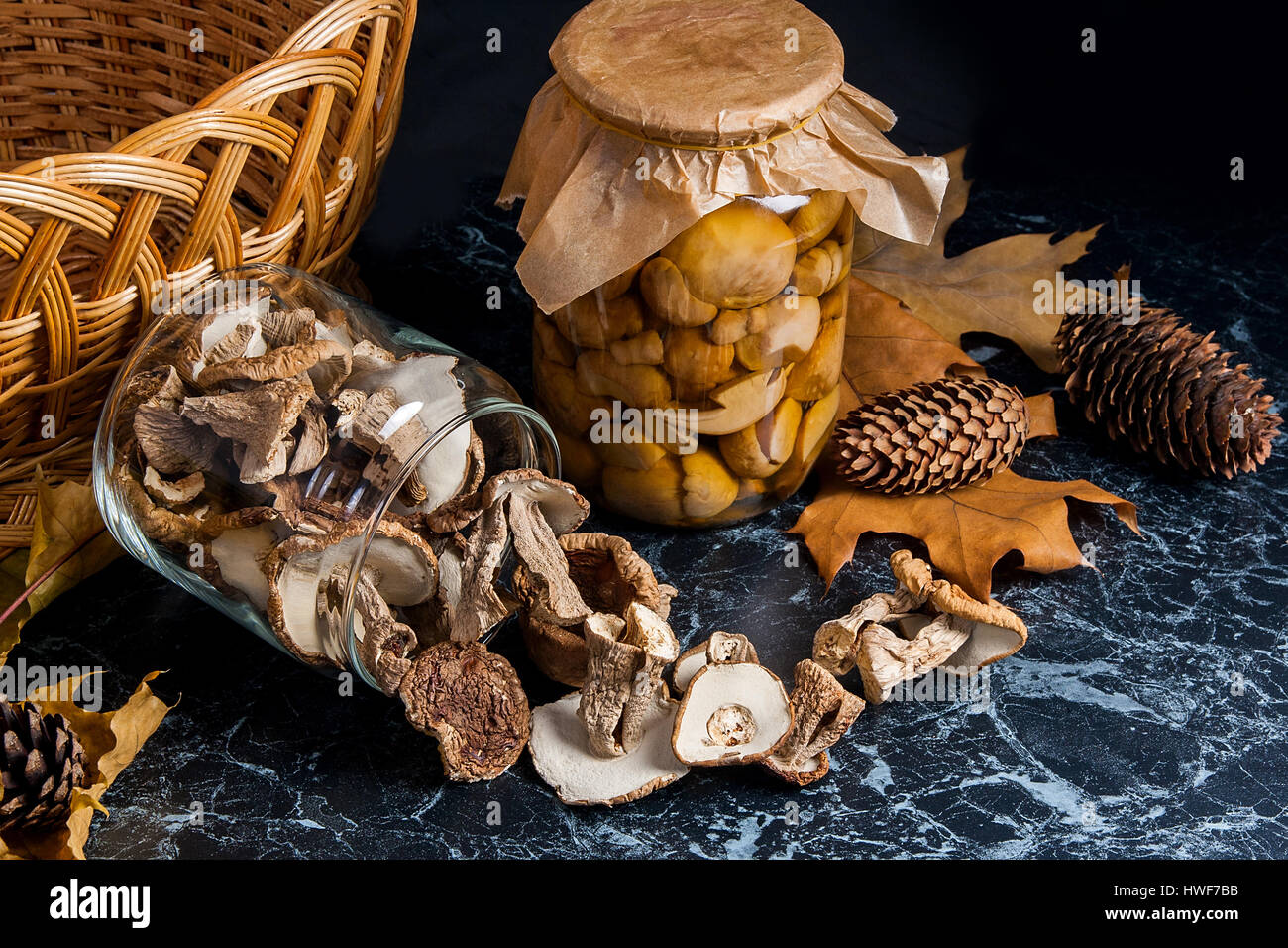 Two glass jars with wild mushrooms on black marble background. One jar