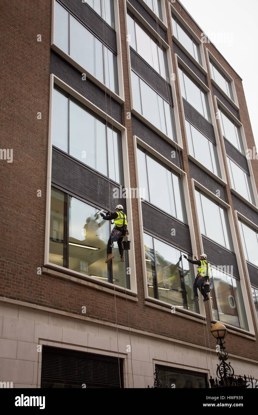 Two window cleaners working while abseiling down a new office block in London Stock Photo