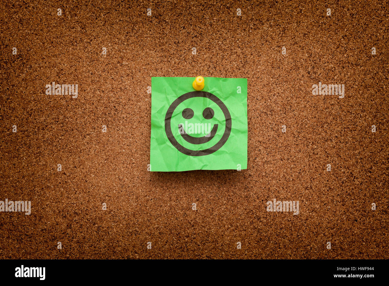 Crumpled green paper with smiling face on corkboard (bulletin board). Stock Photo