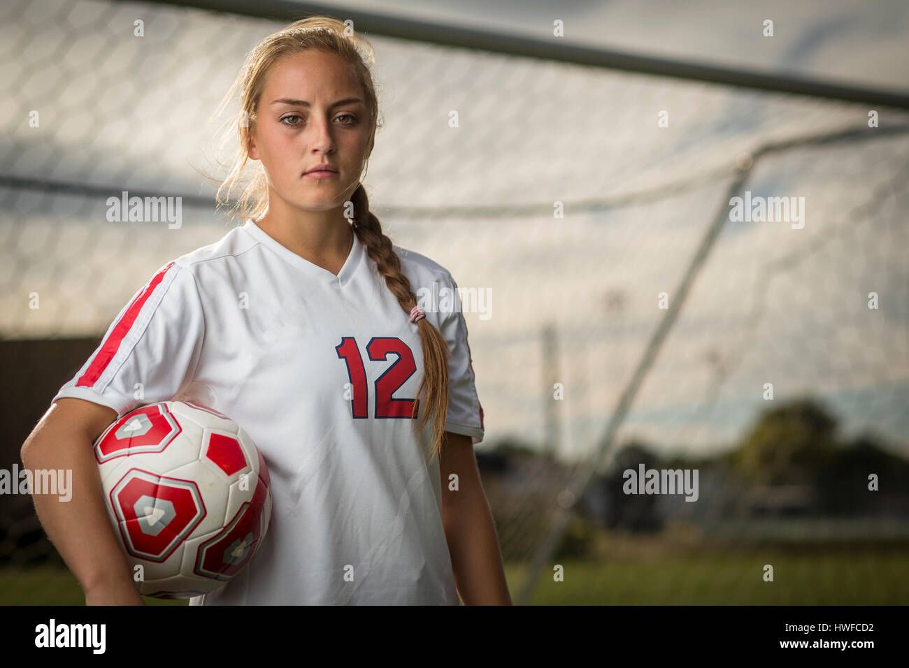 Low angle waist up portrait of serious athlete standing and holding ball in soccer goal Stock Photo