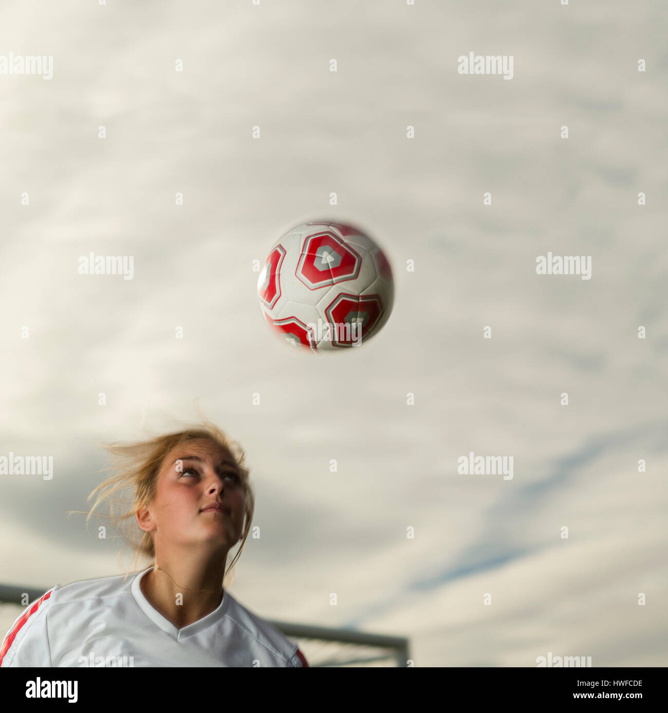 Low angle view of athlete hitting ball with head in soccer goal under cloudy sky Stock Photo