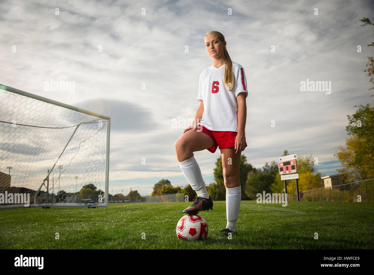 Low angle portrait of athlete standing with soccer ball on field under cloudy sky Stock Photo