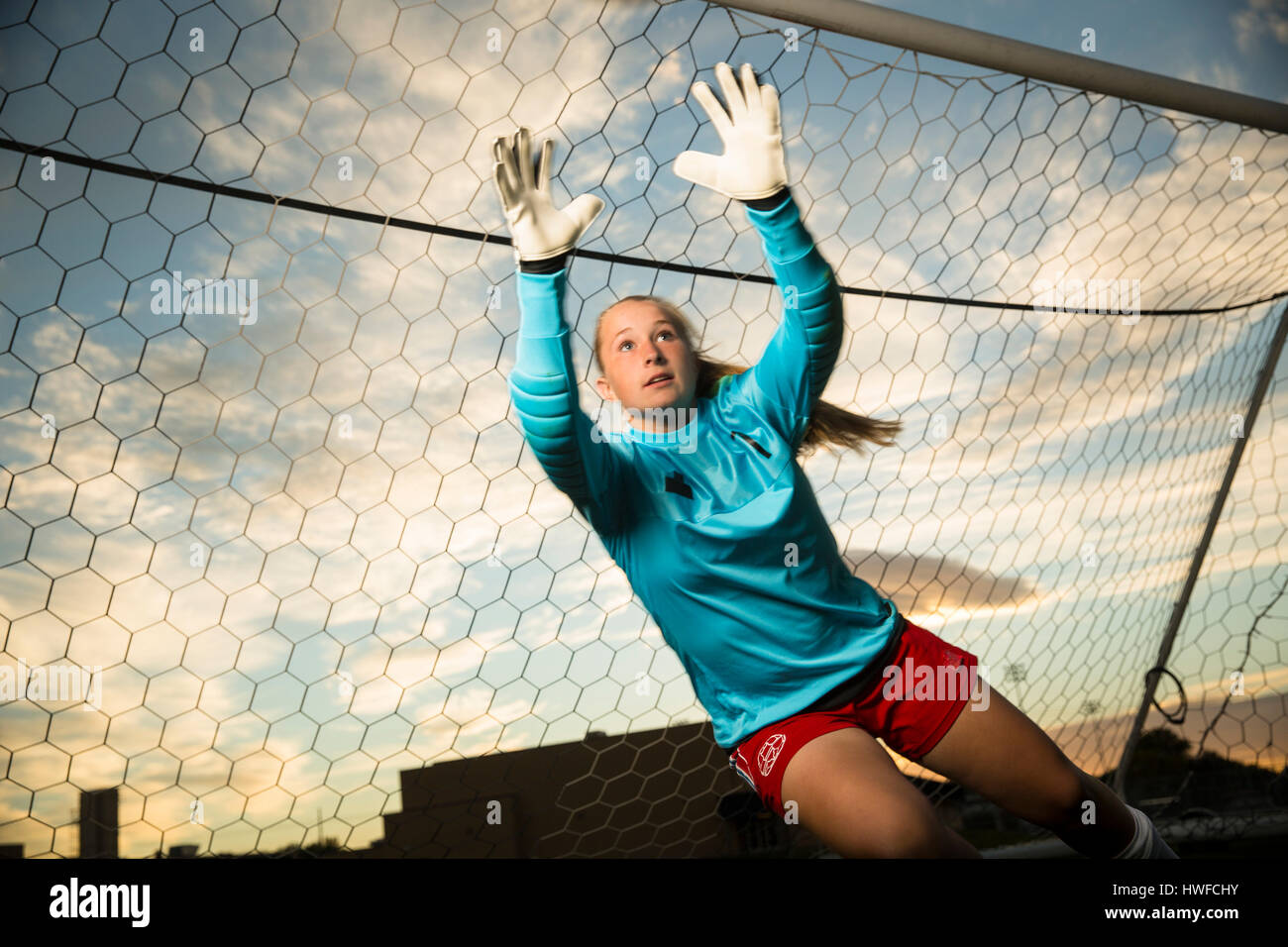 Low angle view of goalie jumping and reaching for soccer ball in goal under blue sky Stock Photo