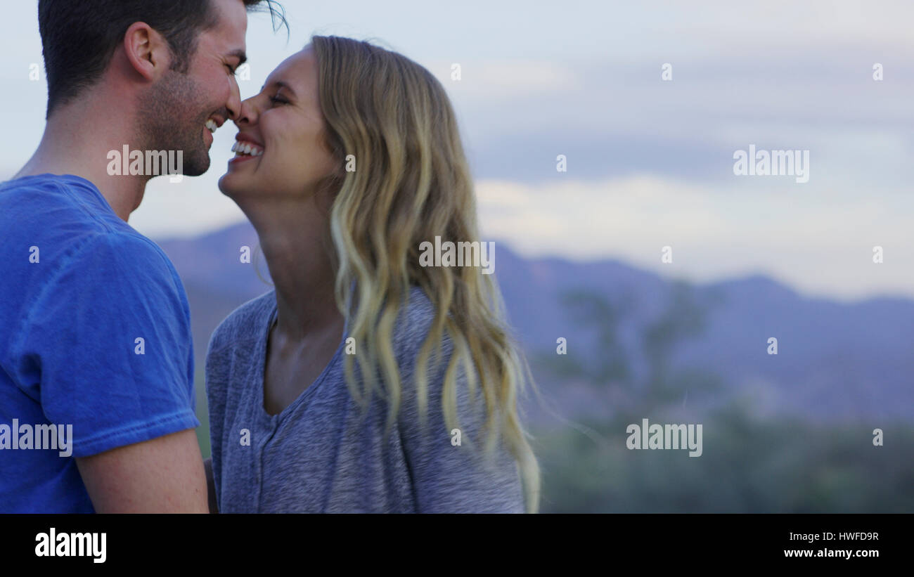 Low angle view of smiling couple touching noses in remote landscape Stock Photo