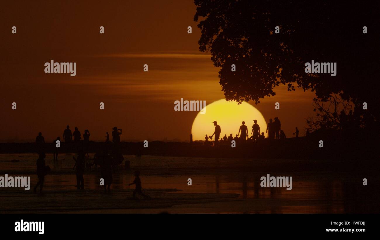 Silhouette of people standing on scenic beach under glowing sun in sunset sky Stock Photo