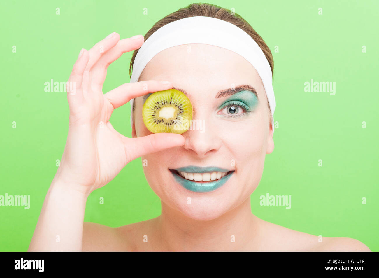 Charming young woman with make-up putting a slice of fresh kiwi on her ...