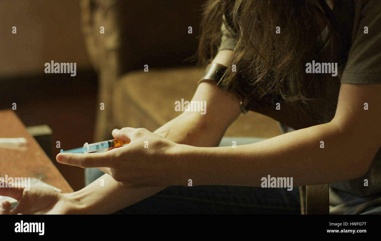 Close up of drug addict injecting drugs in arm with syringe needle and tourniquet on dingy sofa Stock Photo