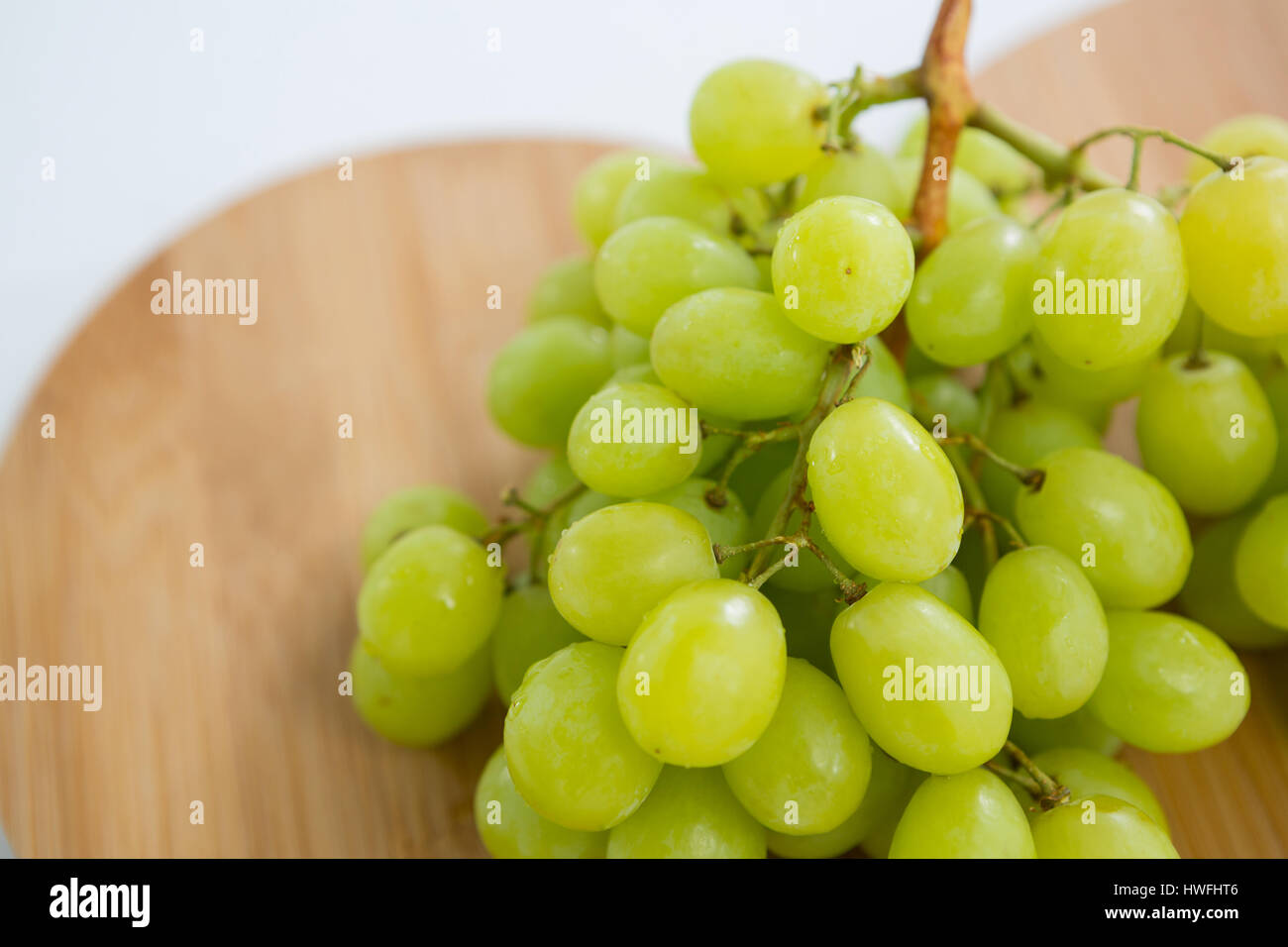Close-up of green bunch of grapes on chopping board against white background Stock Photo