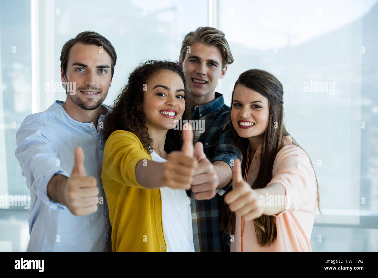 Portrait of smiling creative business team showing thumbs up in office ...