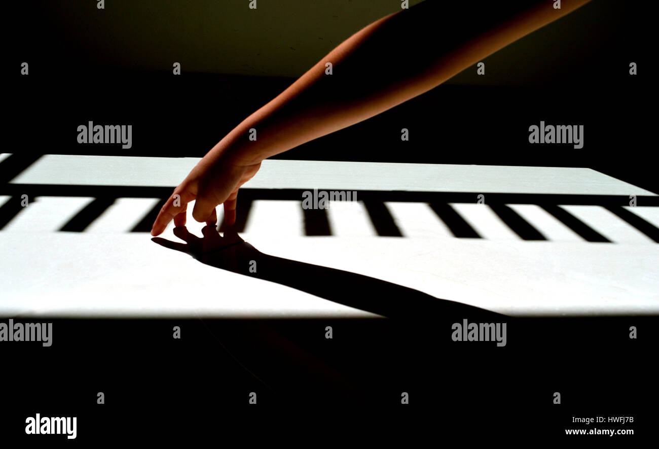 Children's hand playing a piano of light and shadow in the ground Stock Photo