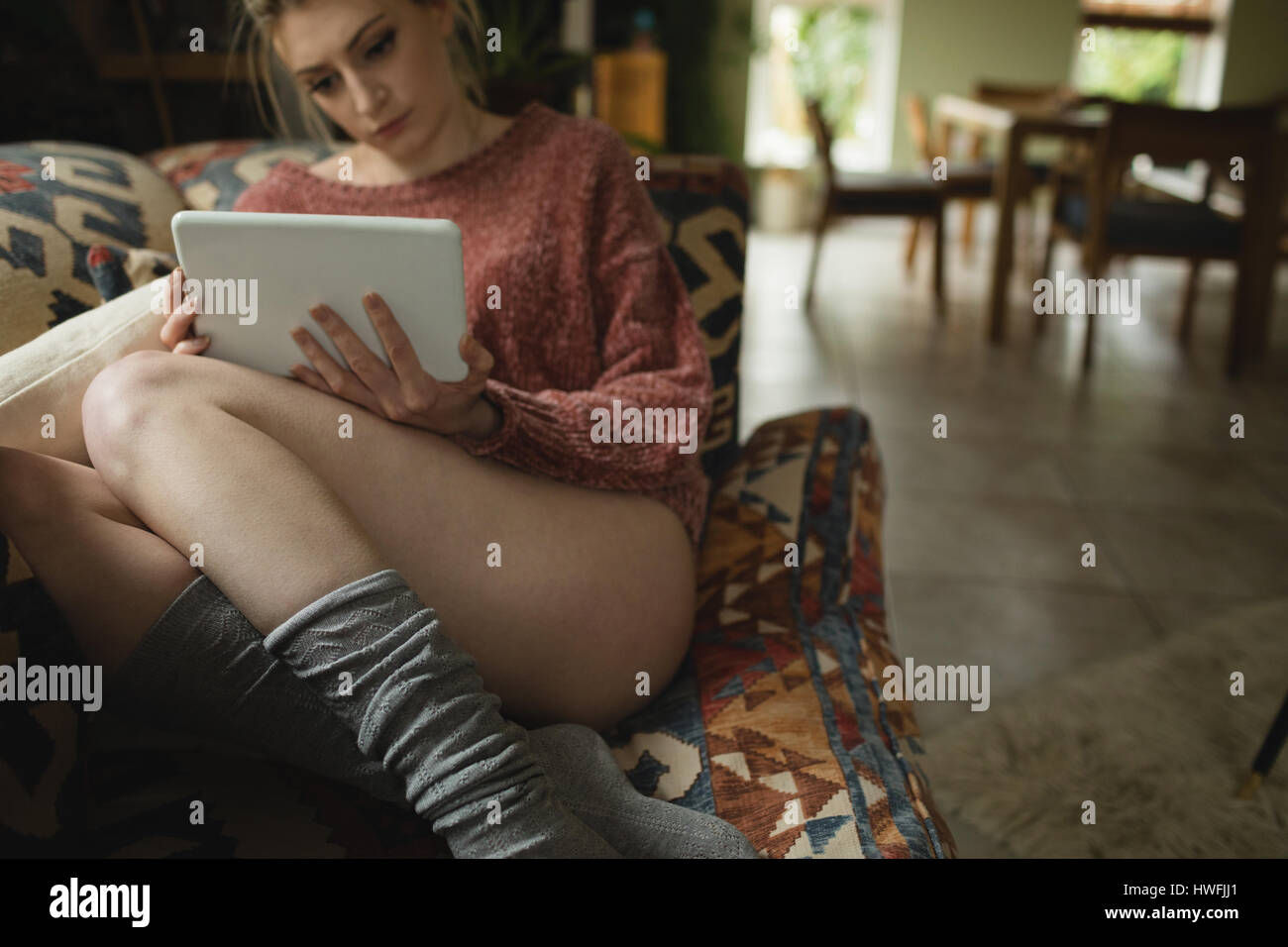 Woman sitting and using digital tablet on couch in living room at home ...