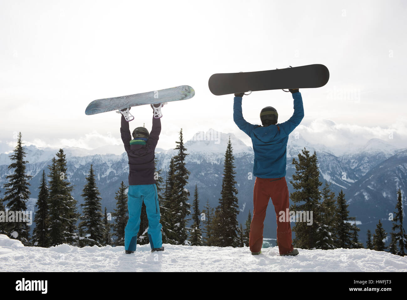 Rear view of man and woman holding snowboard at mountain during winter ...