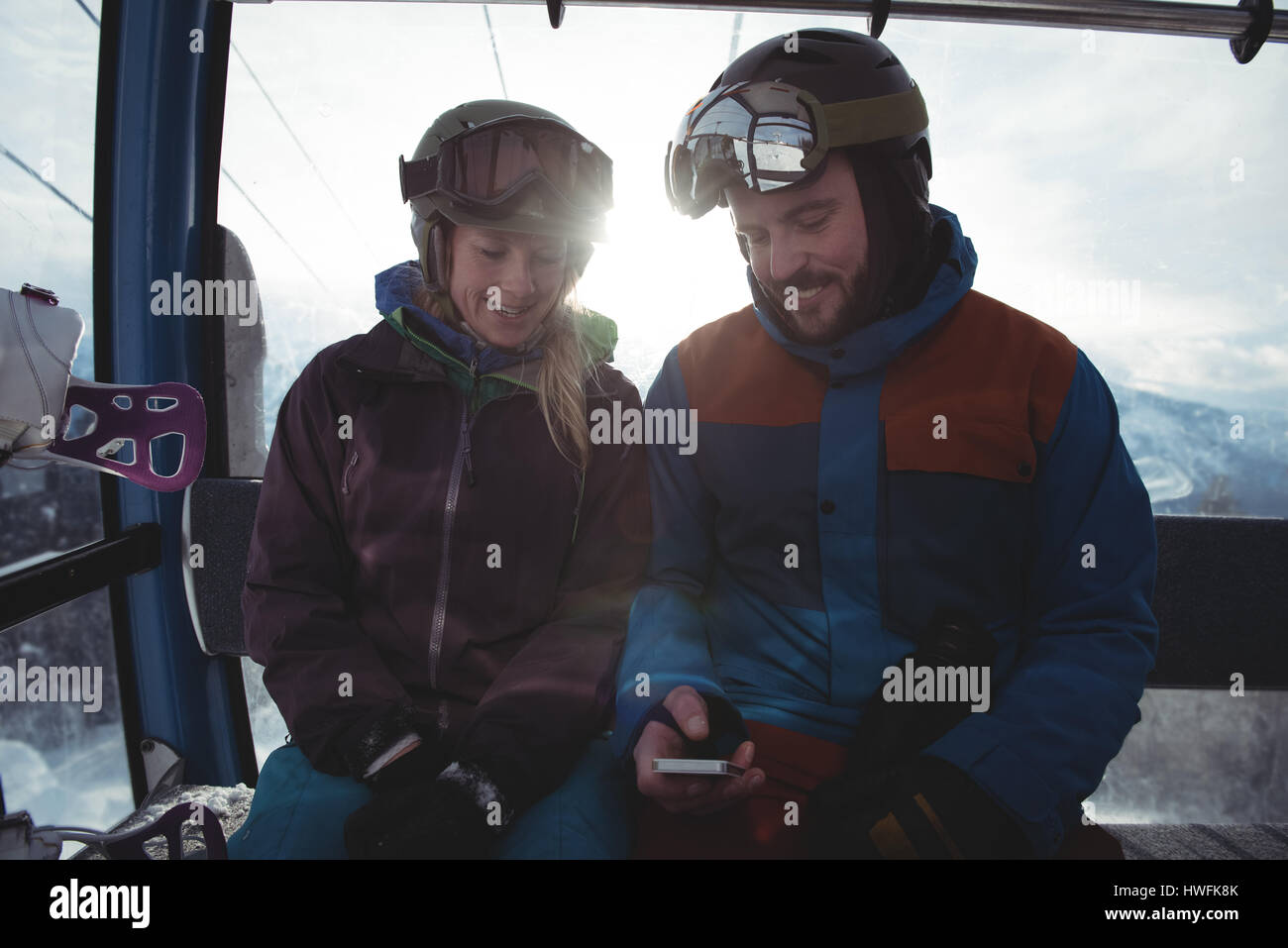 Happy couple using mobile phone while sitting in overhead cable car against sky during winter Stock Photo