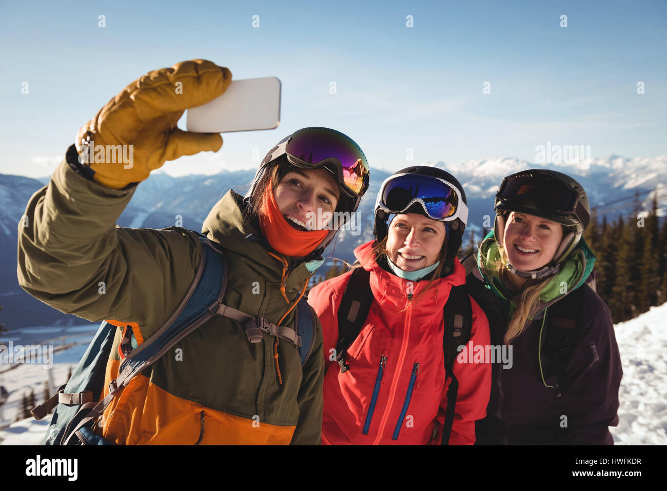 Three smiling female skiers taking selfie on mobile phone during winter Stock Photo