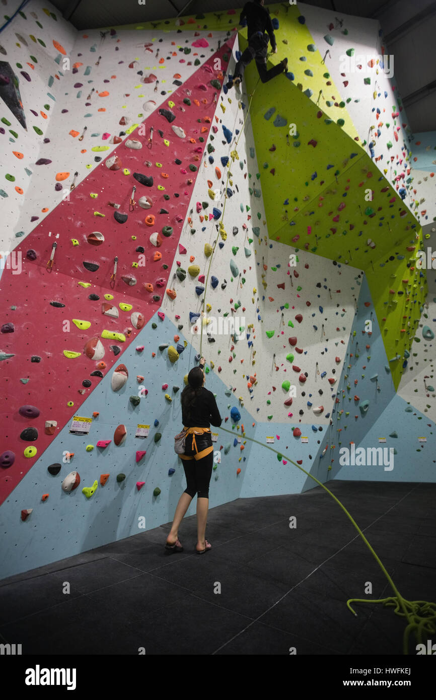 Trainer assisting man while climbing on artificial wall in gym Stock Photo