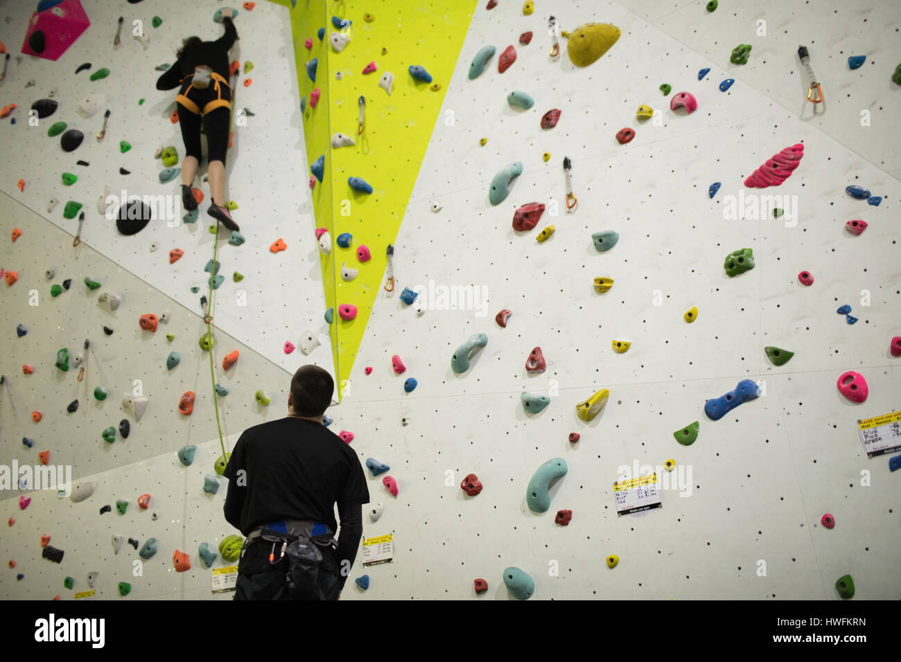 Trainer assisting woman while climbing on artificial wall in gym Stock Photo