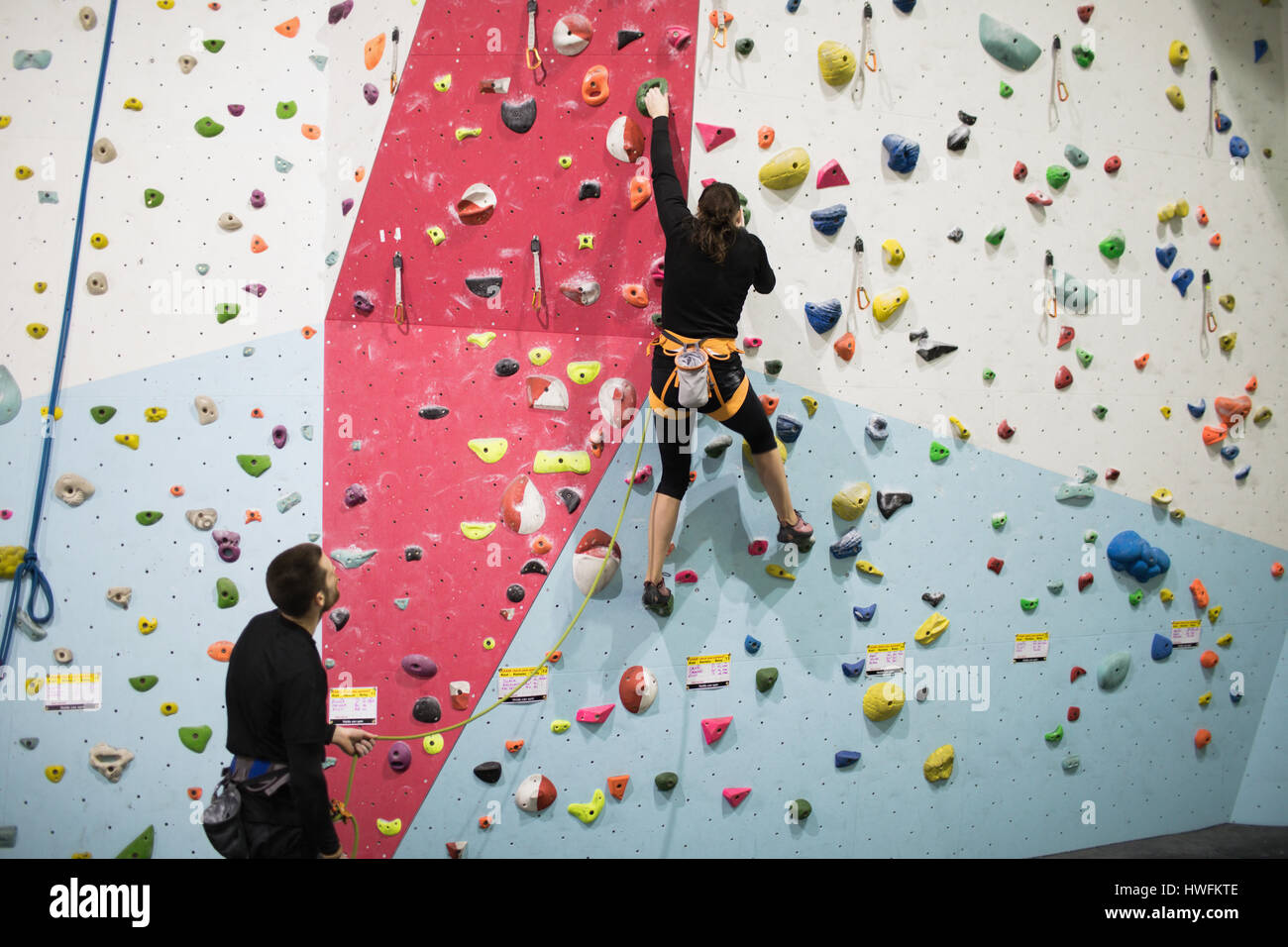 Trainer assisting woman while climbing on artificial wall in gym Stock Photo